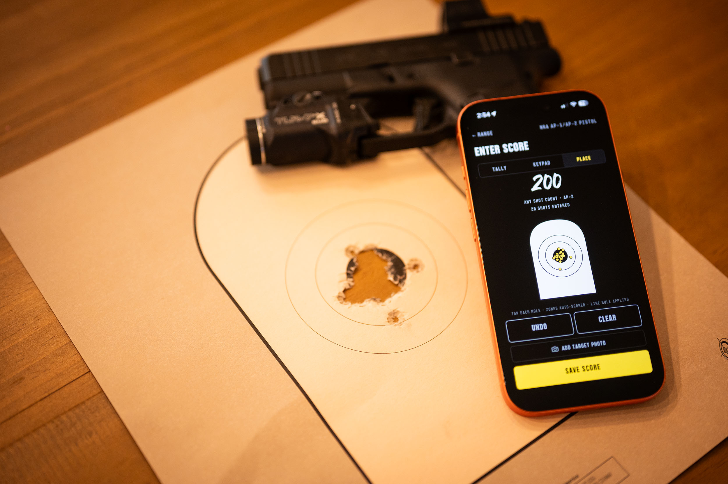 A shot-out AP target and pistol on the bench, with Press scoring the group in PLACE mode